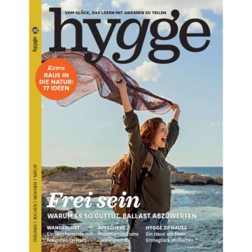Cover des Magazins „Hygge“ mit einer lachenden Person am Meer, die ein Tuch in die Luft hält. Text: „Frei sein - Warum es so guttut, Ballast abzuwerfen“. Zusätzlich Themen wie Wanderlust, Apfelliebe und Hygge zu Hause.